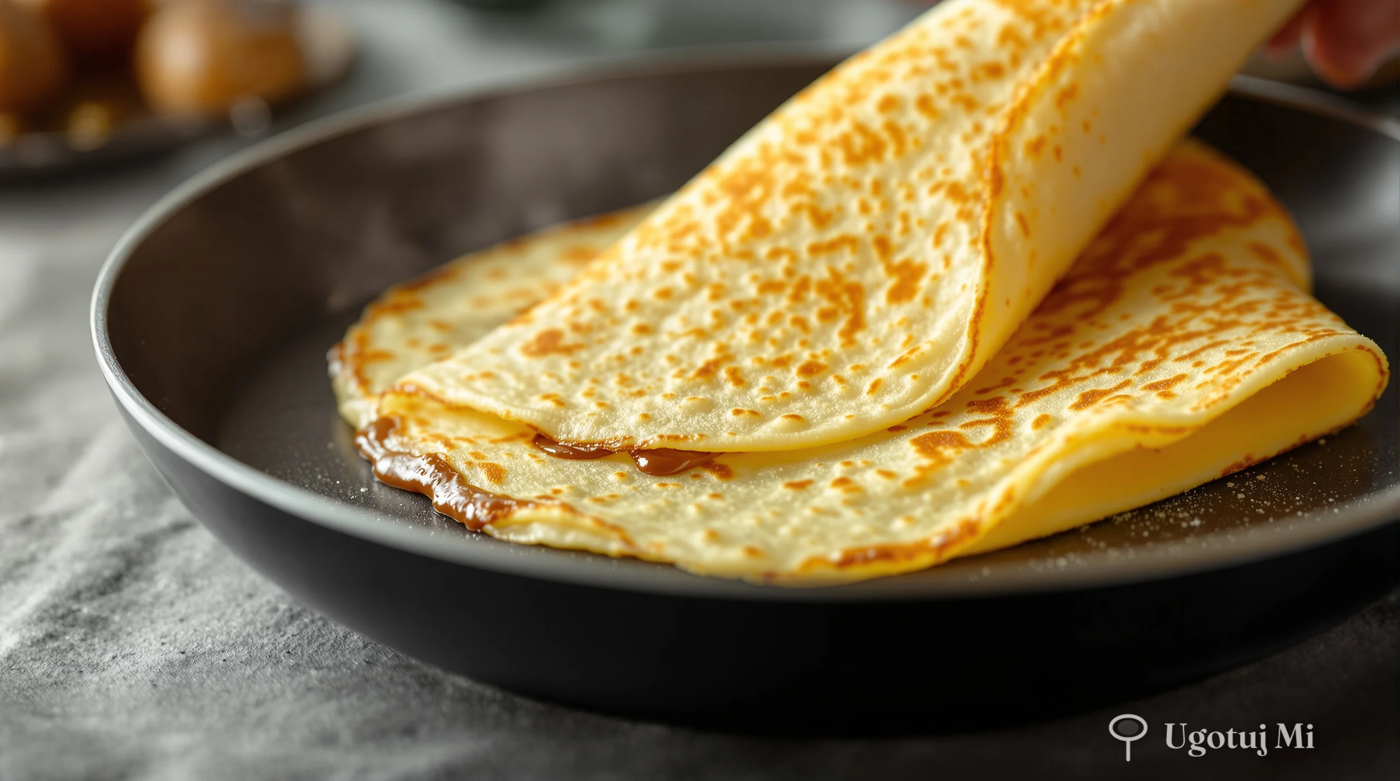 Przewracanie cienkiego naleśnika na patelni - zbliżenie na złocistą powierzchnię | ugotujmi.pl
